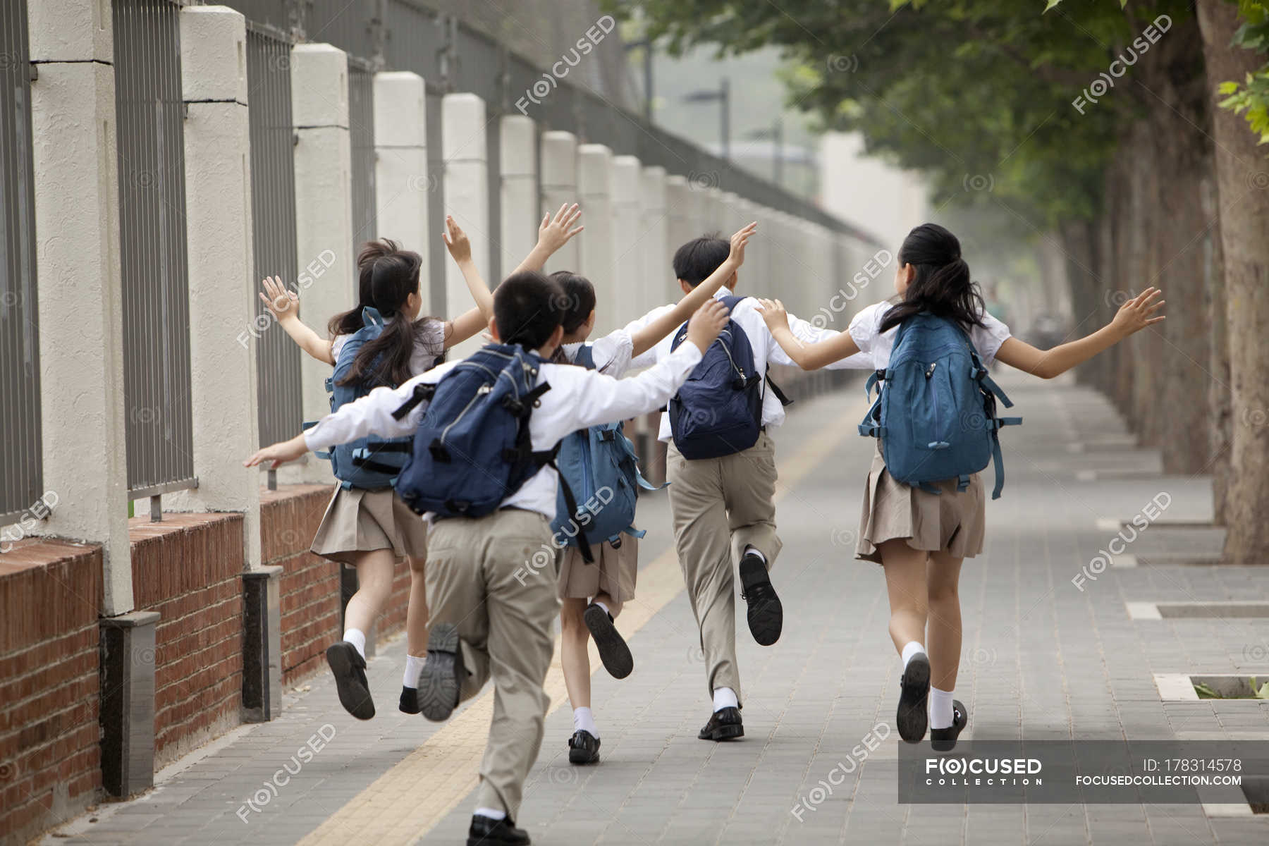 Schoolchildren in school uniform running on sidewalk — backpacks, pre