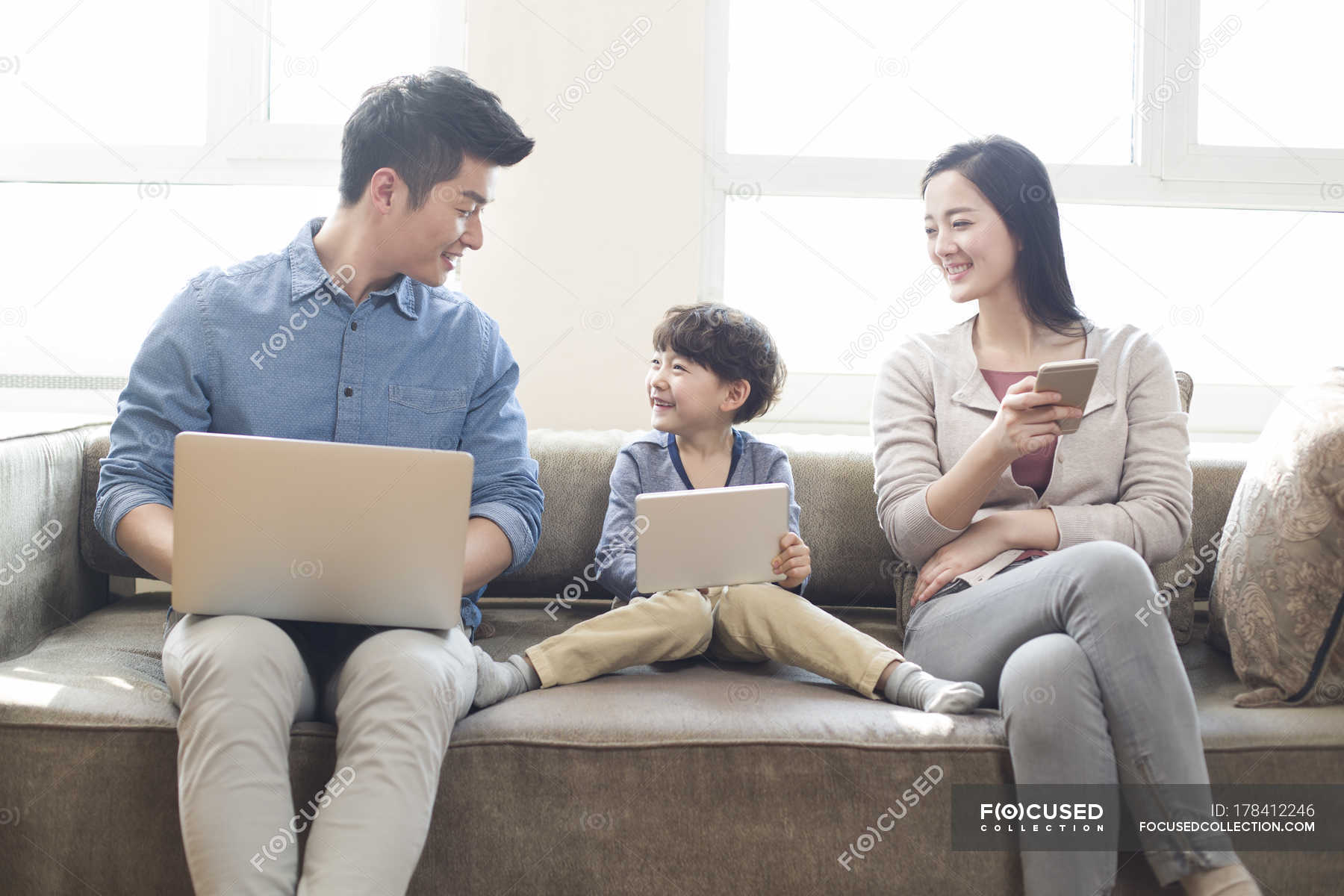 Happy young Chinese family using digital gadgets at home Stock