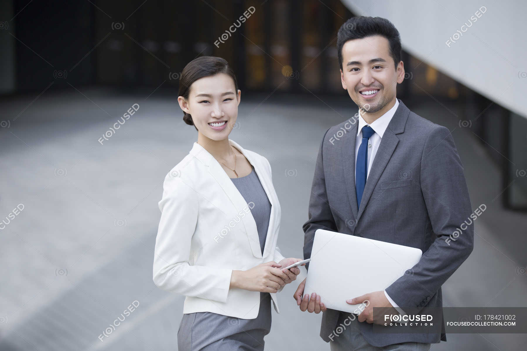 Asian business people standing on street with gadgets and smiling ...