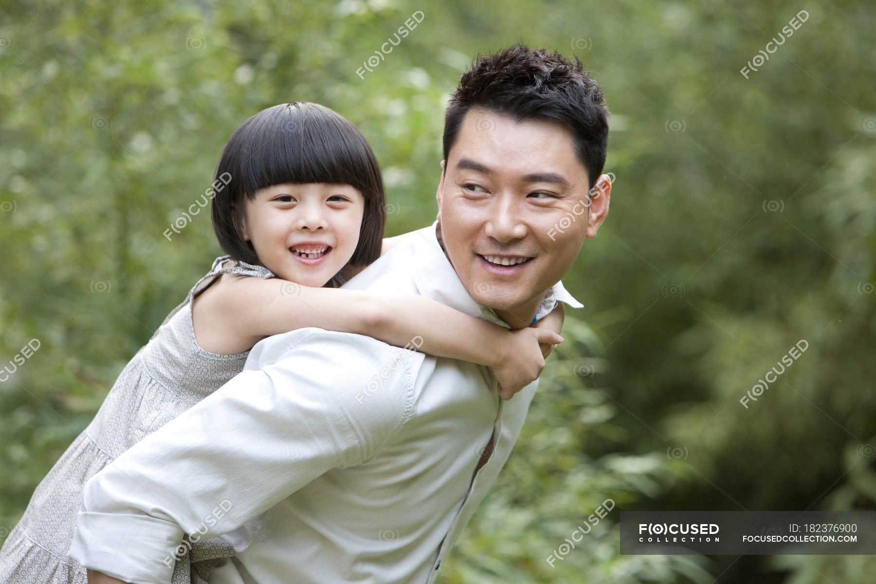 Chinese father giving daughter piggyback ride in garden — selective ...