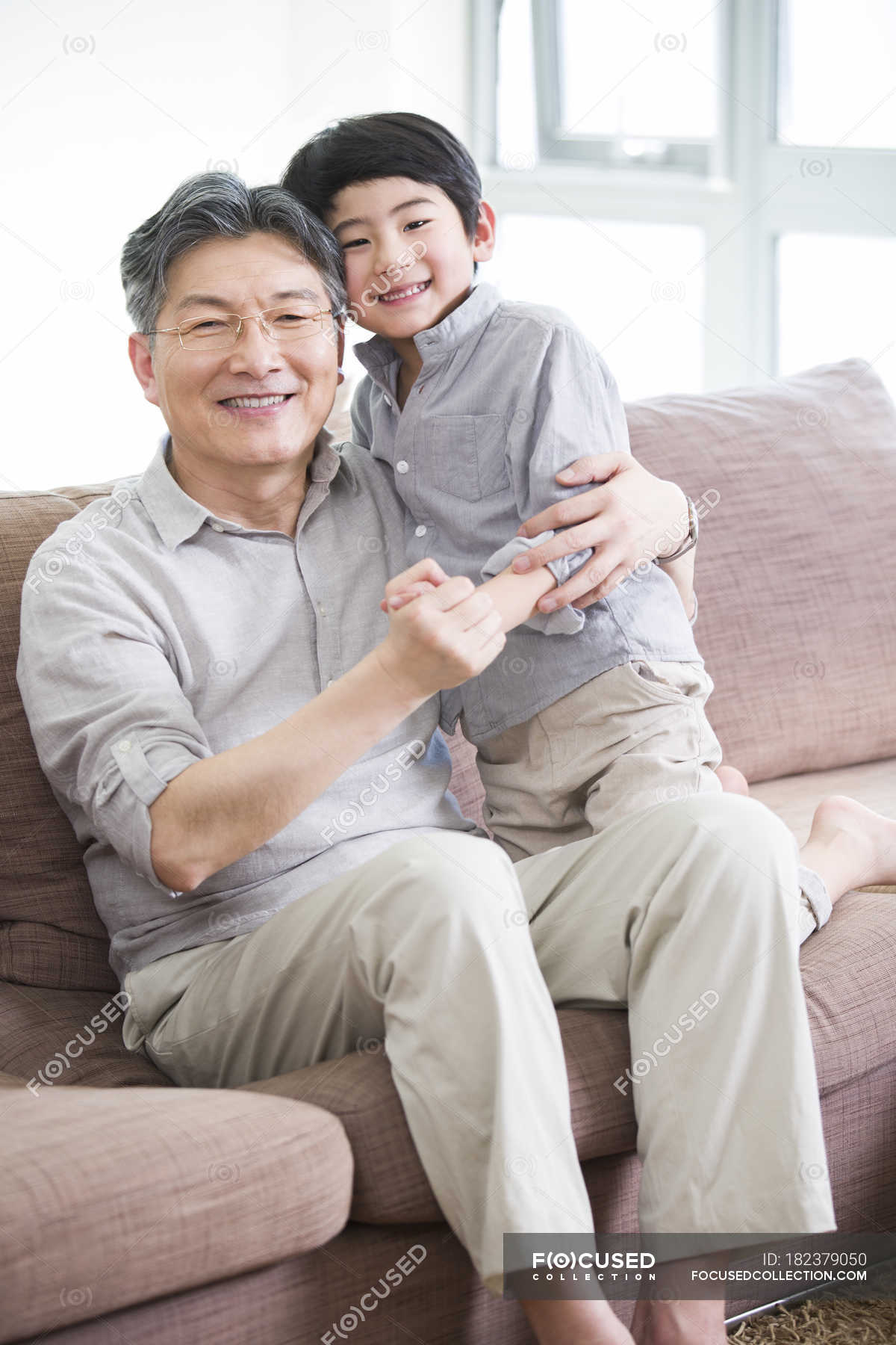 chinese-grandfather-and-grandson-hugging-on-couch-and-smiling-living