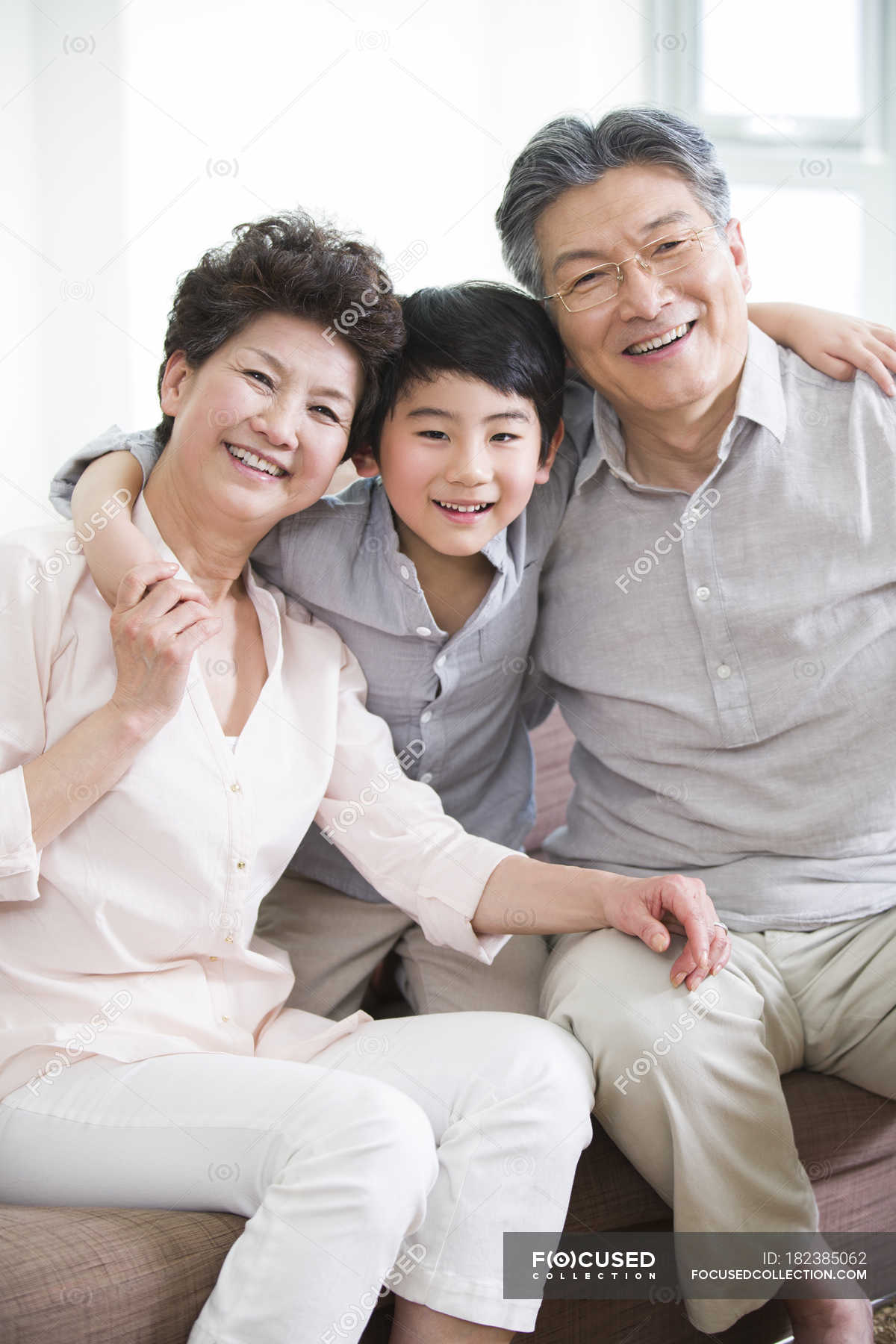 Chinese Grandparents And Grandson Sitting On Sofa Woman Casual Clothing Stock Photo