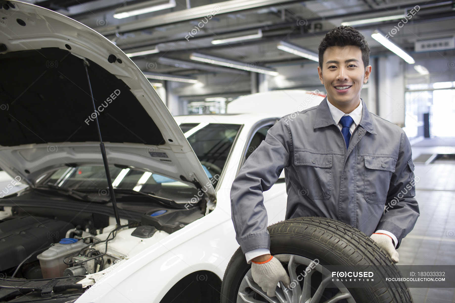 Chinese auto mechanic holding car wheel in — repair shop