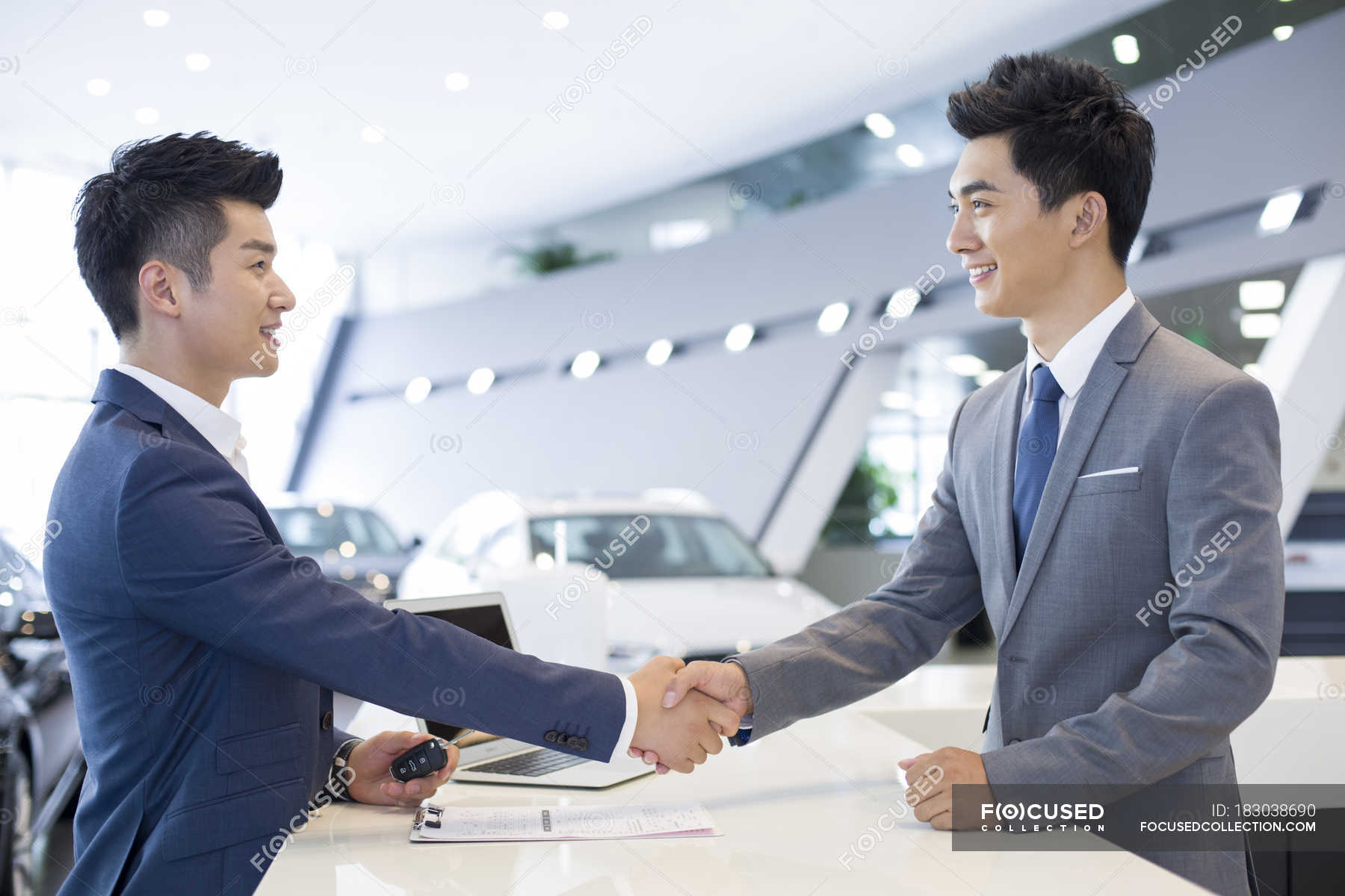 Chinese man shaking hands with car dealer in showroom — keys, client ...