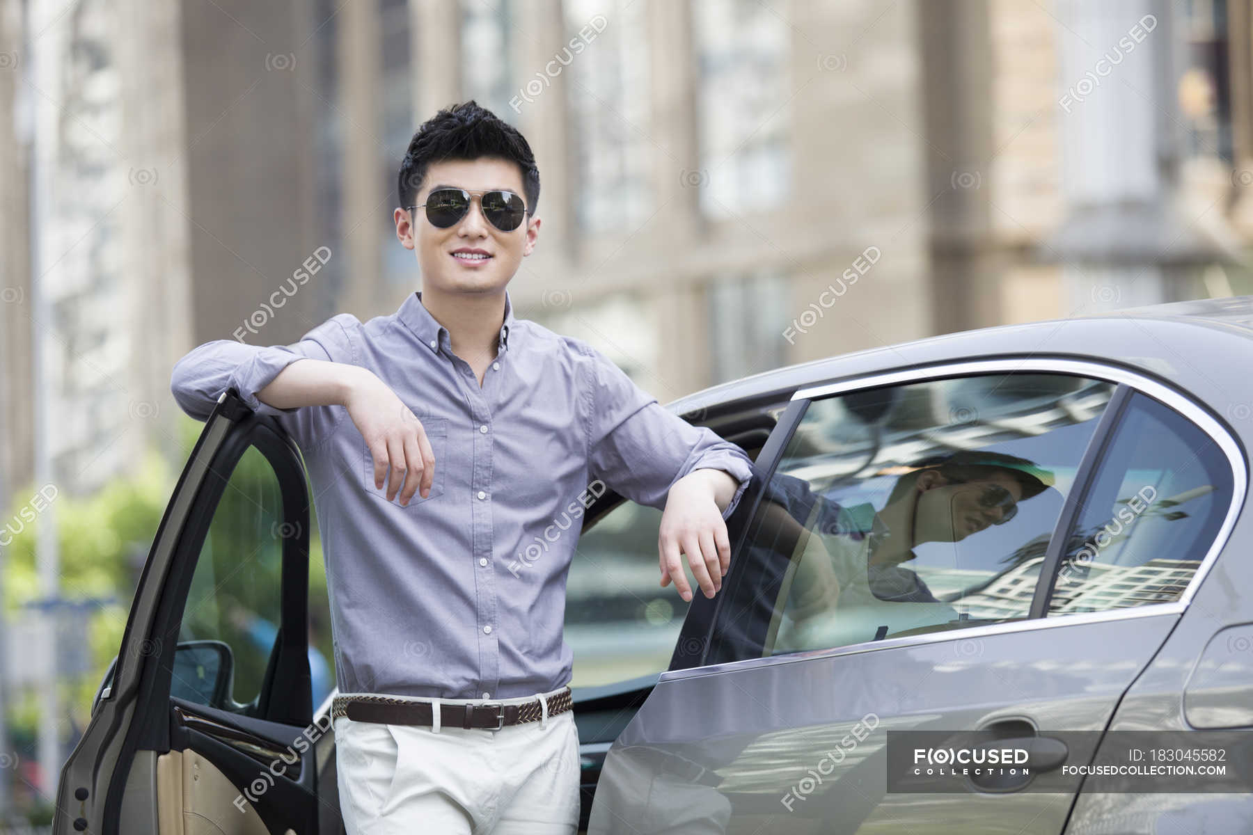 Chinese man standing in front of car in city — looking in camera ...