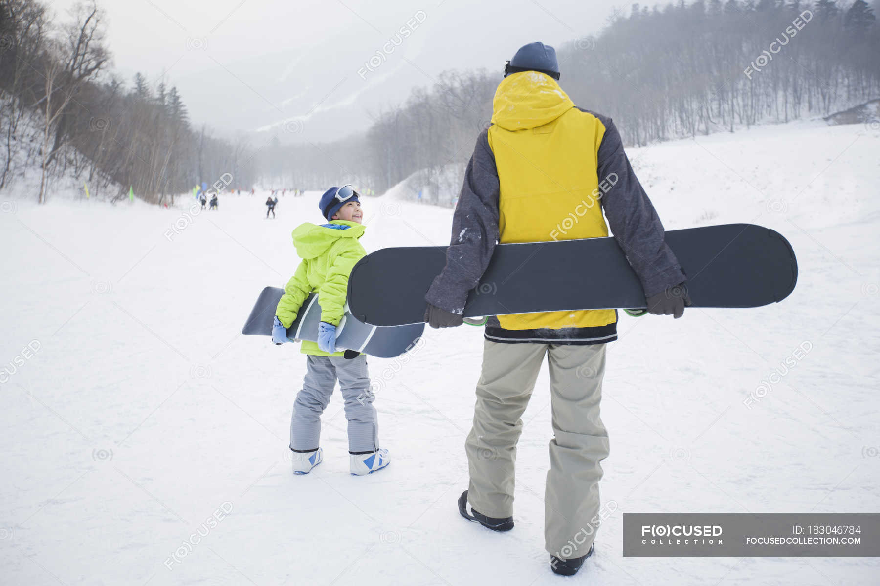 Father and son walking with snowboards on snow — ski resort, boy