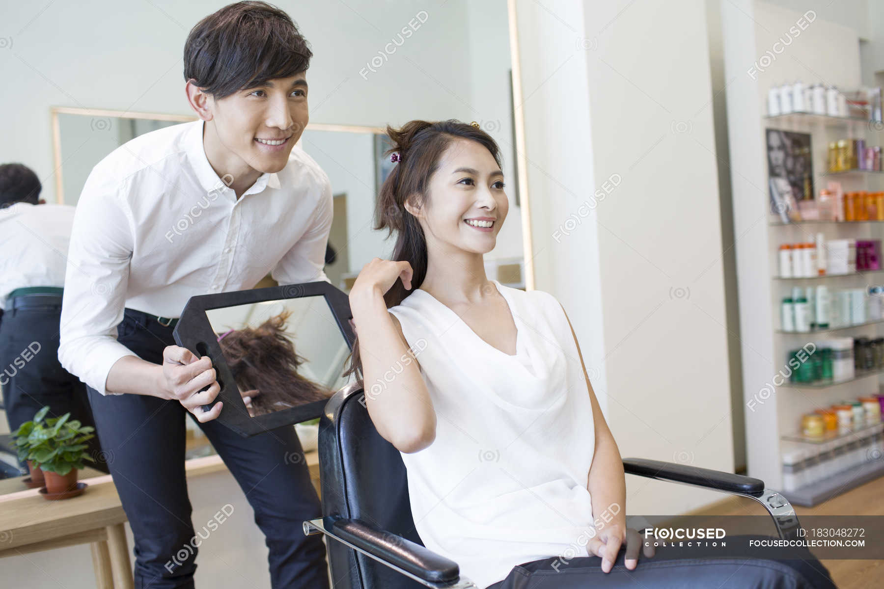 Chinese woman looking in mirror at hair in salon — design, hairdresser -  Stock Photo | #183048272