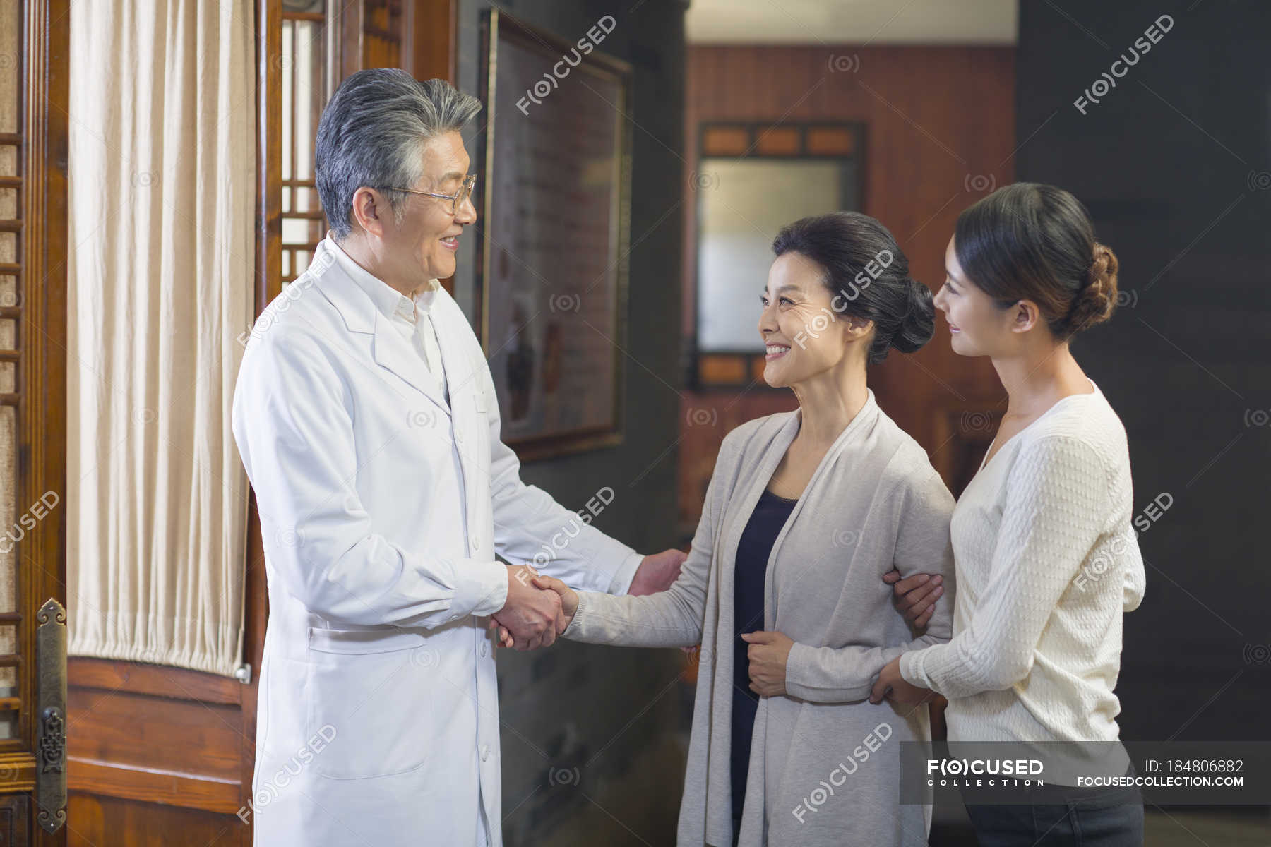 Chinese doctor shaking hands with patients in hospital hall — asian