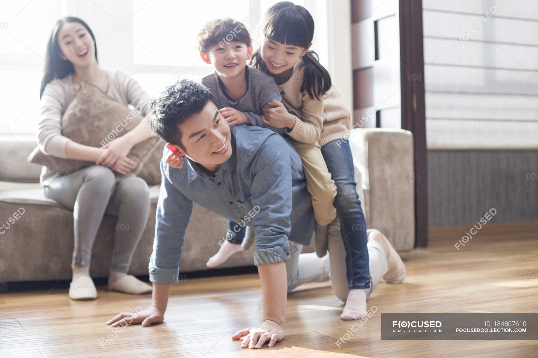 Chinese kids playing with father on floor while mother laughing on sofa ...