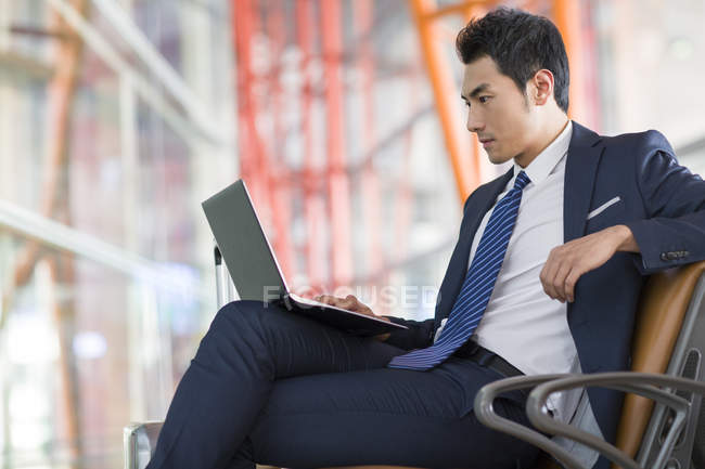 Chinese businessman using laptop in airport waiting room — Stock Photo