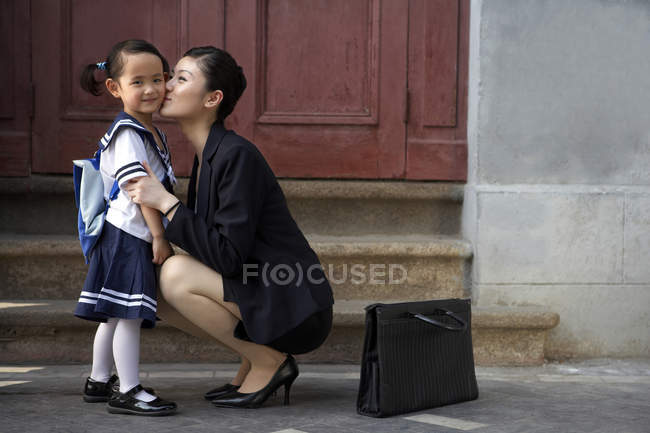 Chinese mother kissing schoolgirl on street — Stock Photo