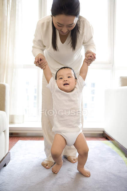 Mujer china ayudando a su hijo caminando en la sala de estar - foto de stock