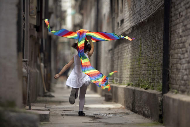 Mädchen läuft mit buntem Drachen in Gasse — Stockfoto