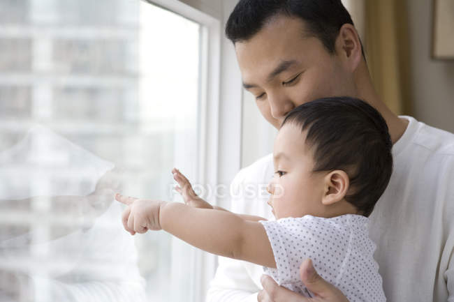 Chinese man with baby boy looking through window and pointing — Stock Photo