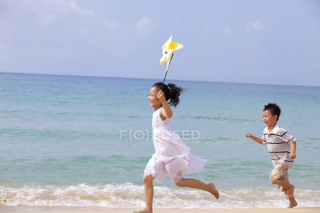 Kinder laufen mit Windrad am Strand — Stockfoto