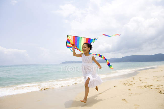 Девушка, бегущая и летящая цветной змей на пляже — стоковое фото