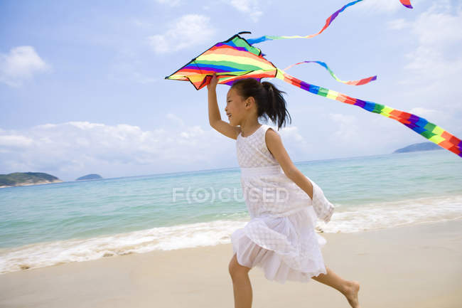 Девушка, бегущая и летящая цветной змей на пляже — стоковое фото
