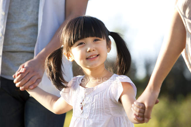 Маленькая китаянка с косичками, держащаяся за руки с семьей на летнем лугу — стоковое фото