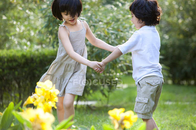 Chinese children holding hands and whirling in garden — Stock Photo