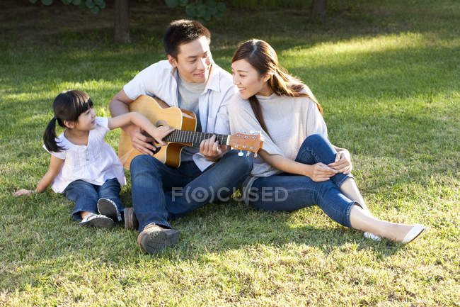 Китаец играет на гитаре с семьей в парке — стоковое фото