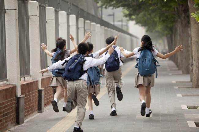 Schoolchildren in school uniform running on sidewalk — Stock Photo