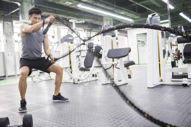 Asian man exercising with battling rope at gym — Stock Photo