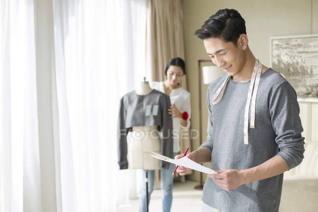 Chinese male fashion designer holding sketches in studio — Stock Photo