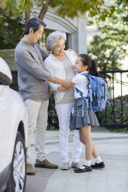 Chinese schoolgirl embracing grandparents at street — Stock Photo