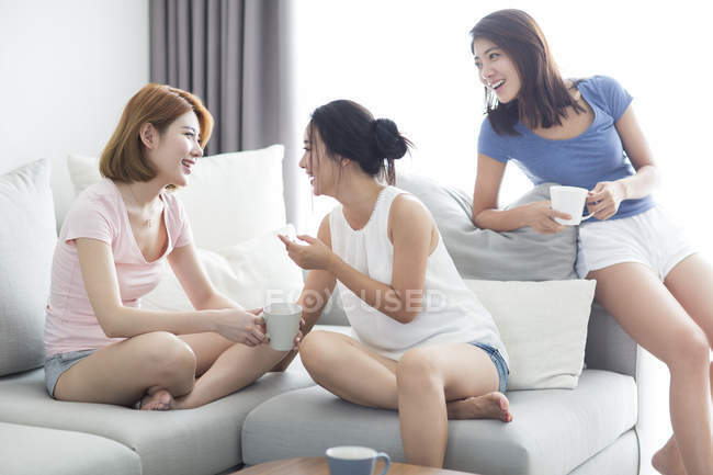 Female friends drinking coffee on sofa — Stock Photo