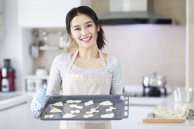 Asian woman holding tray with cookies in kitchen — Stock Photo
