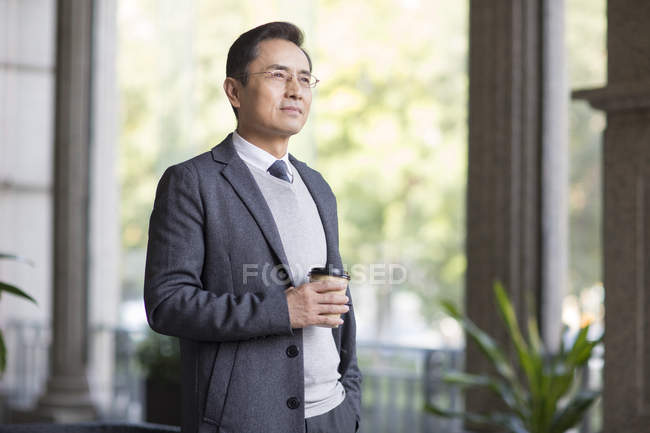 Chinese businessman holding coffee and looking away in city — Stock Photo