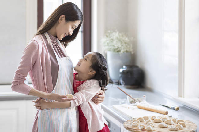 Chinese mother and daughter embracing while making dumplings — Stock Photo