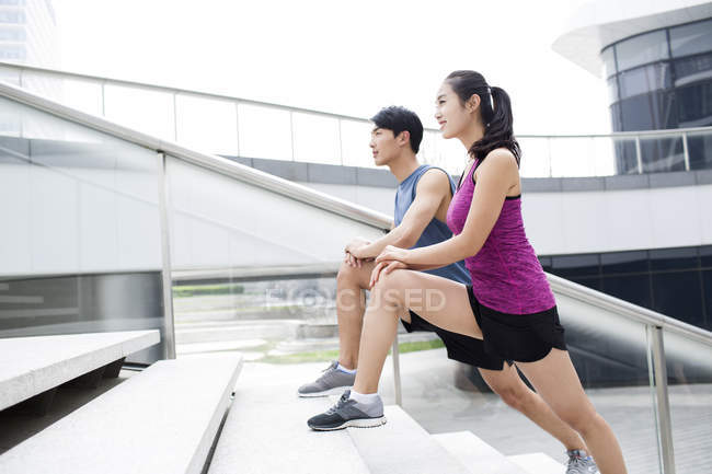 Chinese couple stretching legs on stairs — Stock Photo