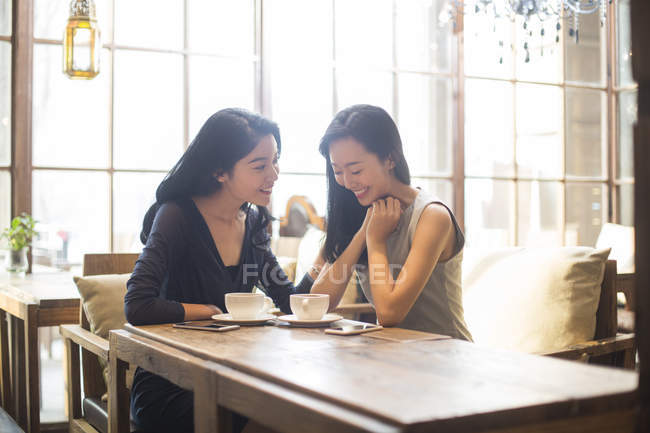 Китайские подруги разговаривают с кофейными чашками в кафе — стоковое фото