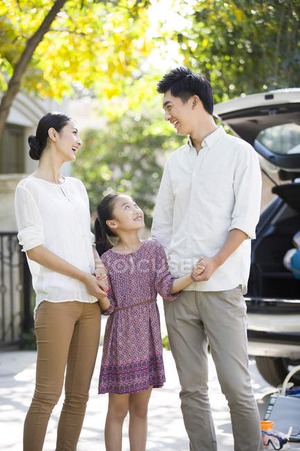 Chinese parents holding hands with daughter in front of car with open trunk — Stock Photo