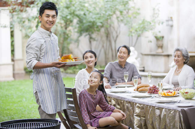 Uomo cinese che tiene mais grigliato per la famiglia multi-generazione nel cortile — Foto stock