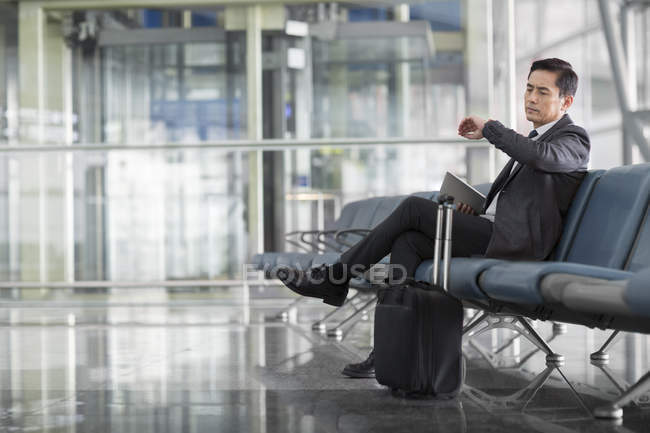 Asiático homem esperando no aeroporto e olhando para relógio de pulso — Fotografia de Stock