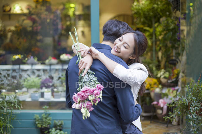 Chinese woman hugging boyfriend with flowers — Stock Photo
