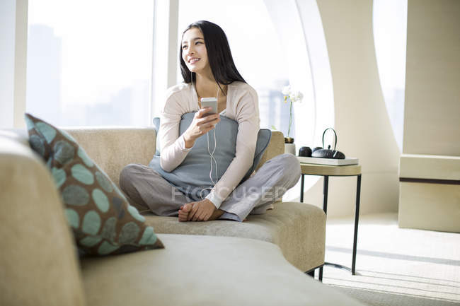 Donna cinese che ascolta musica sul divano in casa interna — Foto stock