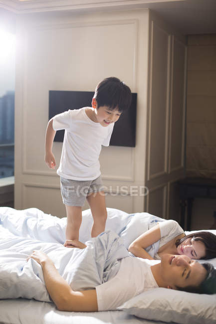 Chinese boy waking up parents in bedroom — Stock Photo