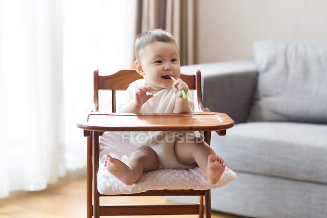 Китайский мальчик сидит в высоком кресле и жует игрушку — стоковое фото