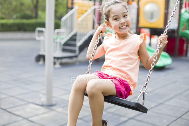 Chinois fille assis sur swing et souriant — Photo de stock