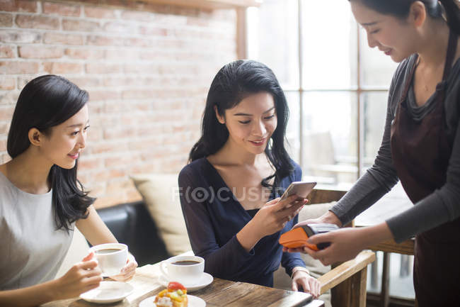Chinese female friends paying with smartphone in coffee shop — Stock Photo