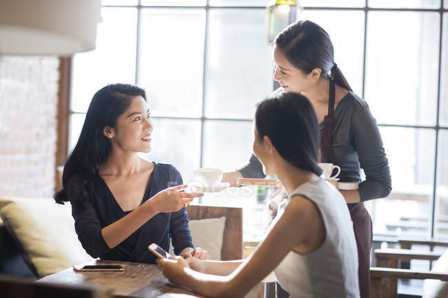 Chinese waitress serving coffee to female friends in cafe — Stock Photo