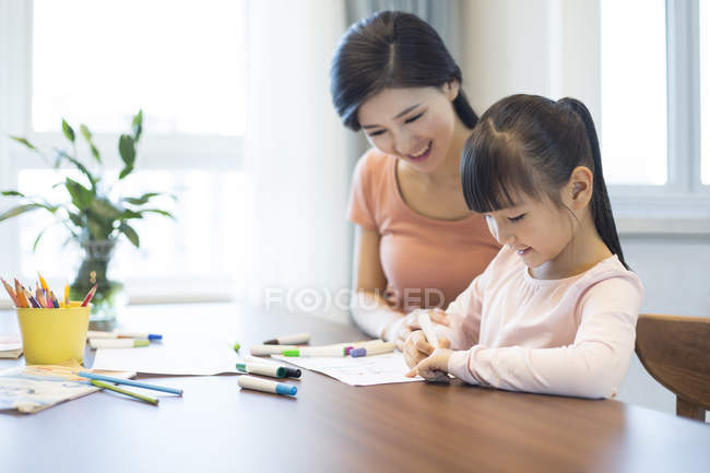 Madre e hija chinas dibujando en la mesa - foto de stock