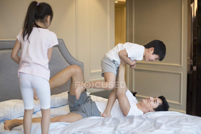 Pai chinês brincando e levantando crianças na cama — Fotografia de Stock