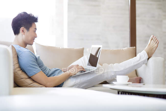 Young Chinese man using laptop on sofa — Stock Photo