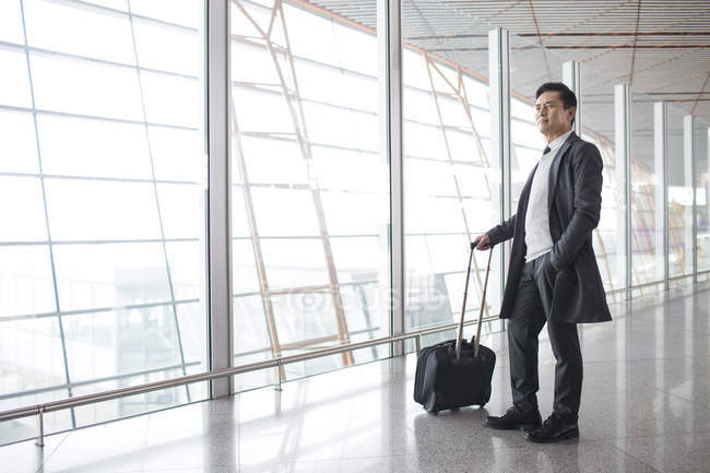 Asian man standing with wheeled luggage in airport lobby — Stock Photo