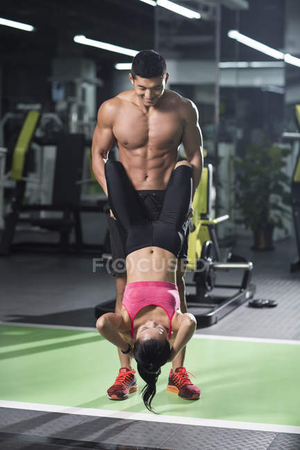 Hombre chino ayudando a la mujer a hacer ejercicio en el gimnasio - foto de stock