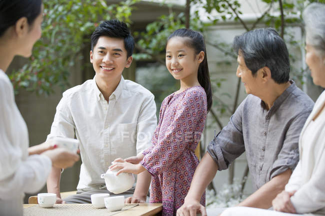 Chinese girl serving tea for multi-generation family in courtyard — Stock Photo